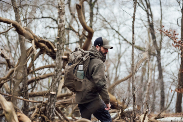 Mann mit Helikon-Tex Rucksack und Thermosflasche wandert durch winterlichen Wald