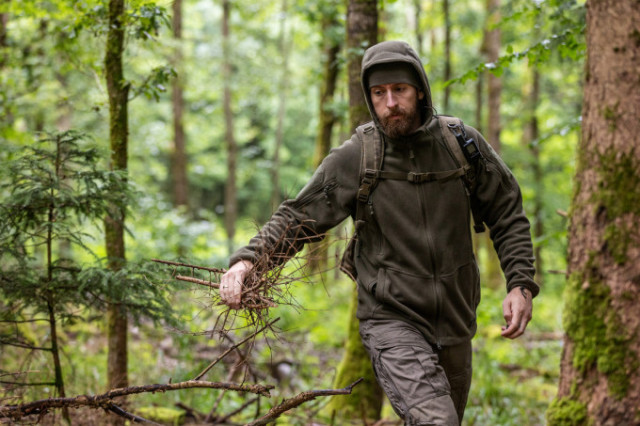 Mann mit Helikon-Tex Hoodie und Rucksack sammelt Holz im Wald