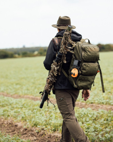 Ein Jäger mit Rucksack und Tarngewehr auf weitem Feld – moderne taktische Jagdausrüstung von TACWRK im Einsatz.
