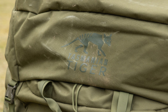 Detailaufnahme des Tasmanian Tiger Logos auf olivfarbenem Rucksackmaterial.